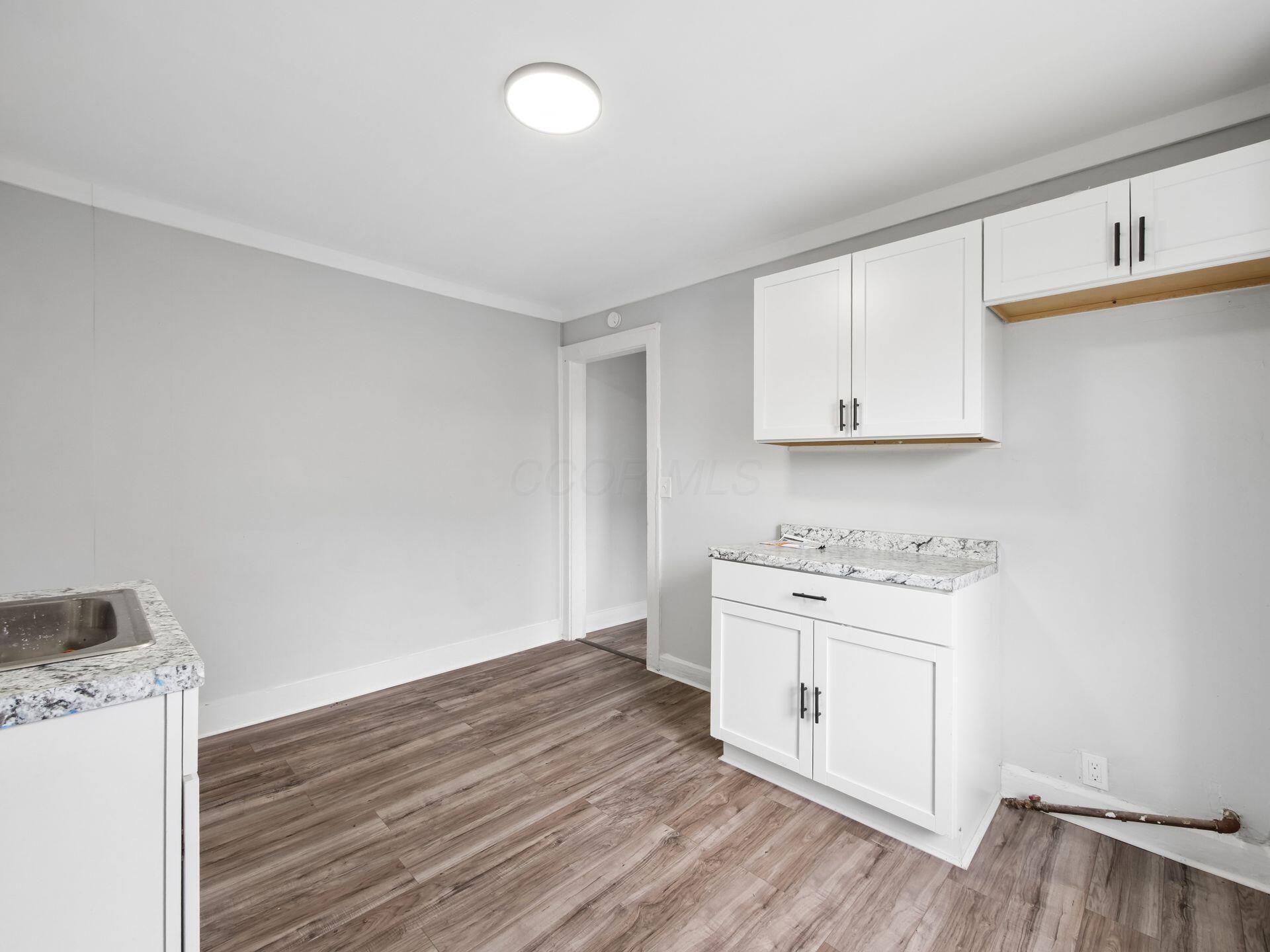 Kitchen with white cabinets, marble-pattern counters, a stainless-steel sink, and wood-look flooring.