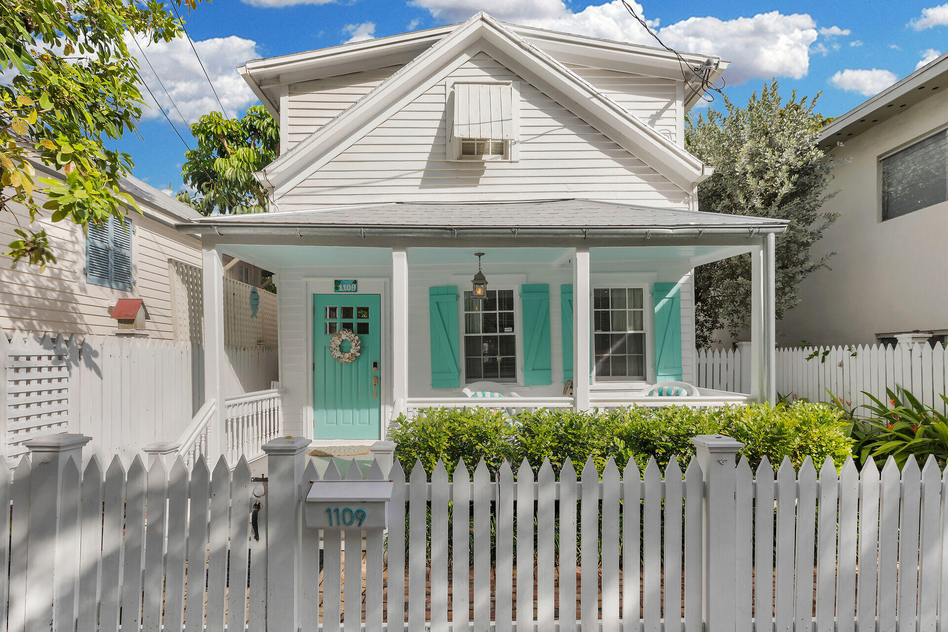 White two-story house with a turquoise door and shutters behind a white picket fence.