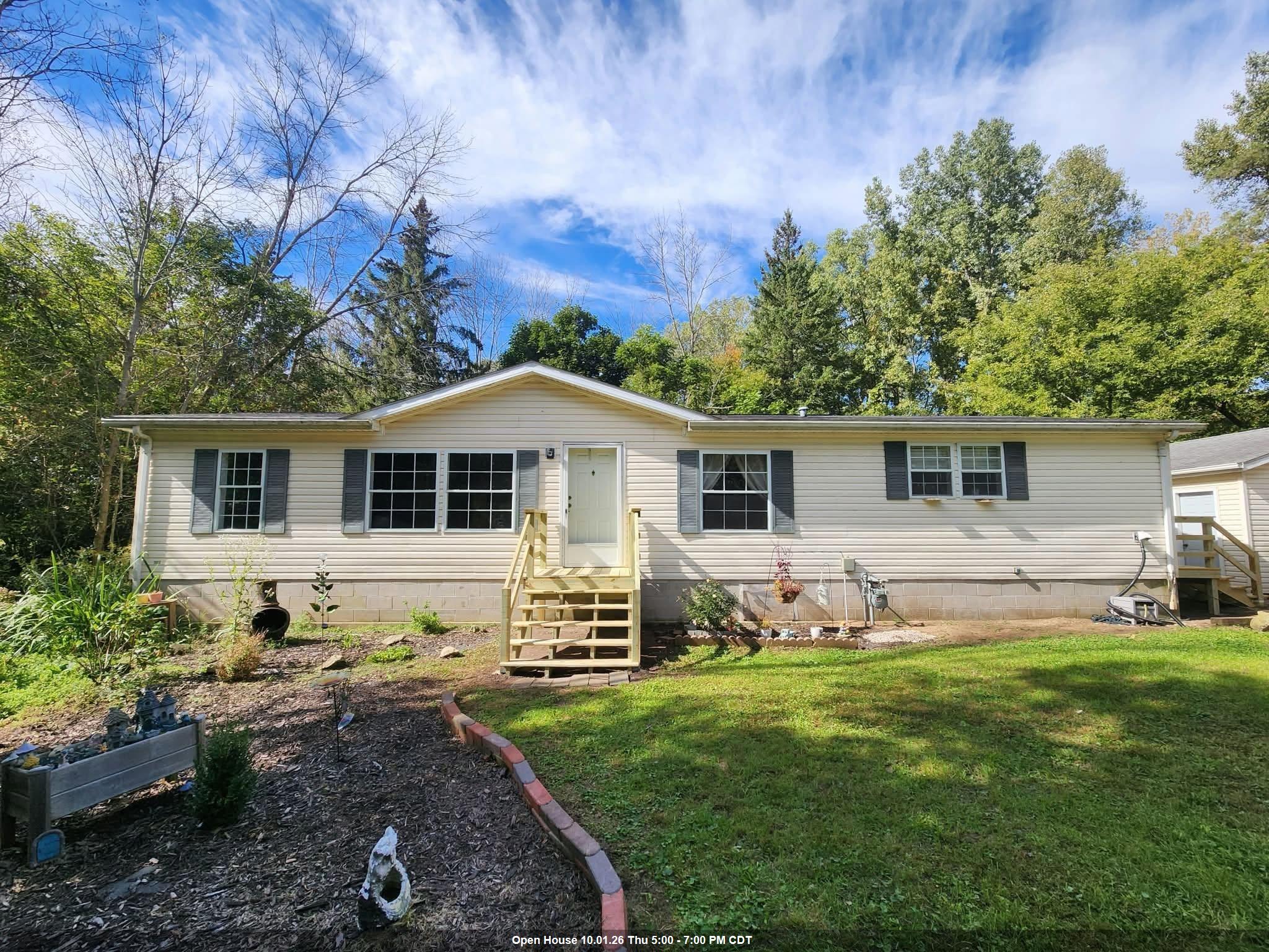 Single-story beige home with central wooden steps, a front lawn, and landscaped garden.