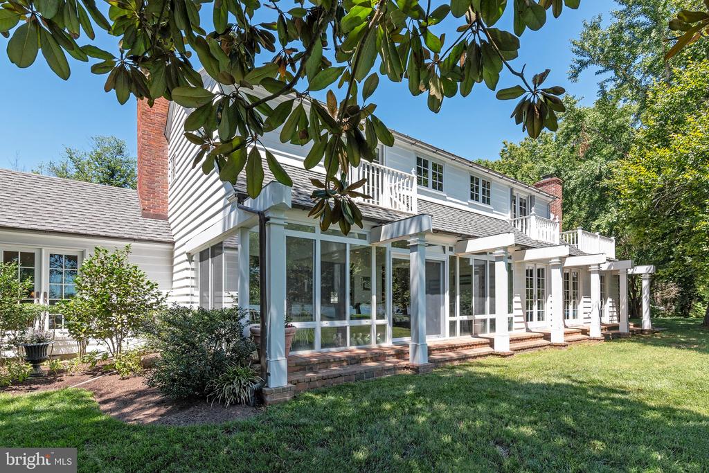 White two-story house with a glass sunroom, upper balcony, and covered patio overlooking a lawn.
