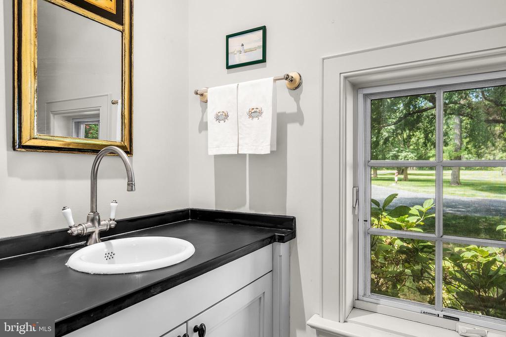 Bathroom vanity with a black countertop and oval sink beside a window overlooking trees and lawn.