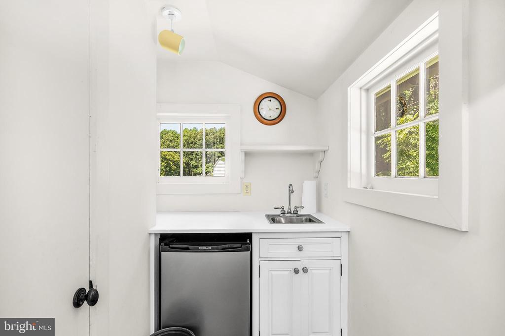 Compact white kitchen with stainless-steel dishwasher, small sink, and two windows overlooking greenery.