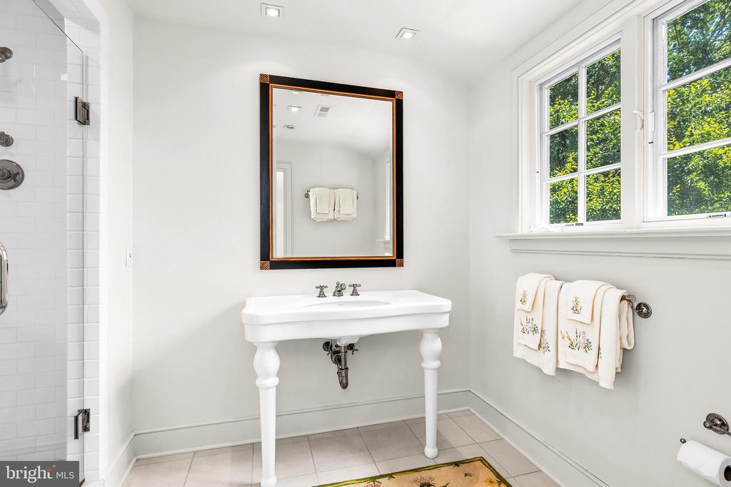 Bathroom with a white pedestal sink, dark-framed mirror, tiled shower, and large windows.