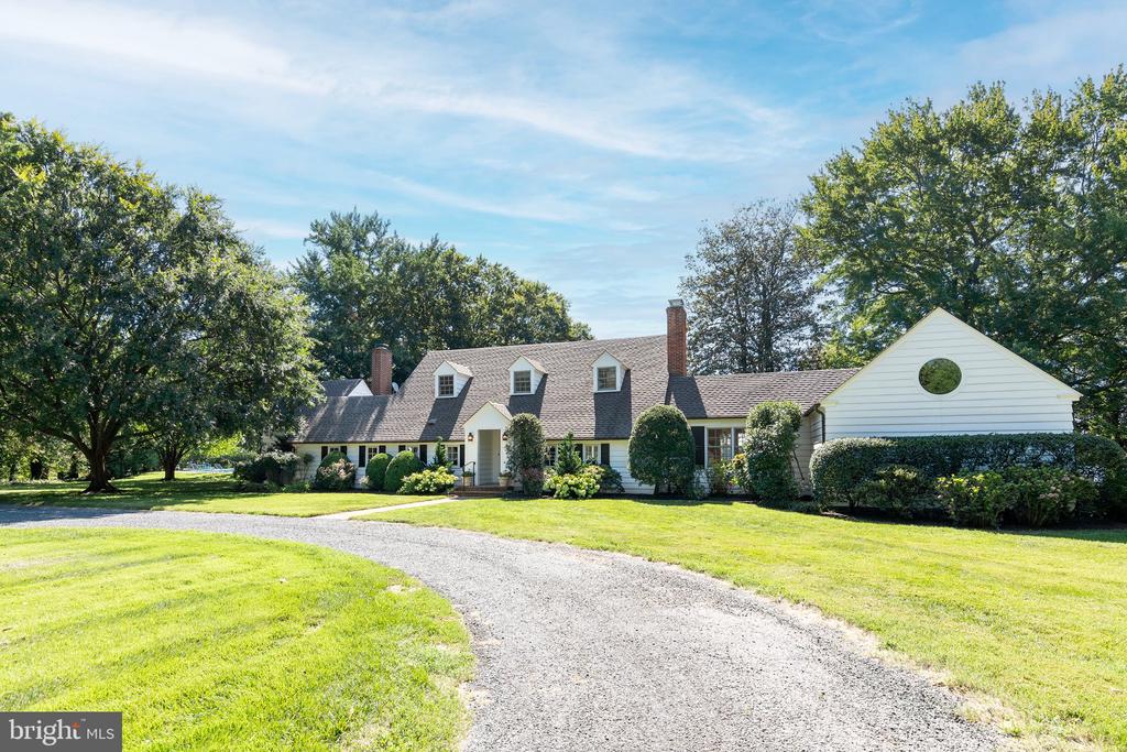 White home with dormers and brick chimneys behind a curved gravel driveway and spacious lawn.
