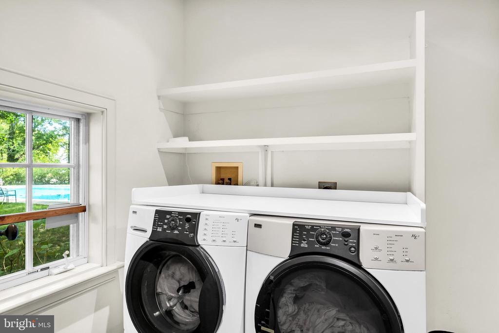 Laundry room with two front-loading appliances beneath built-in shelves beside a window.