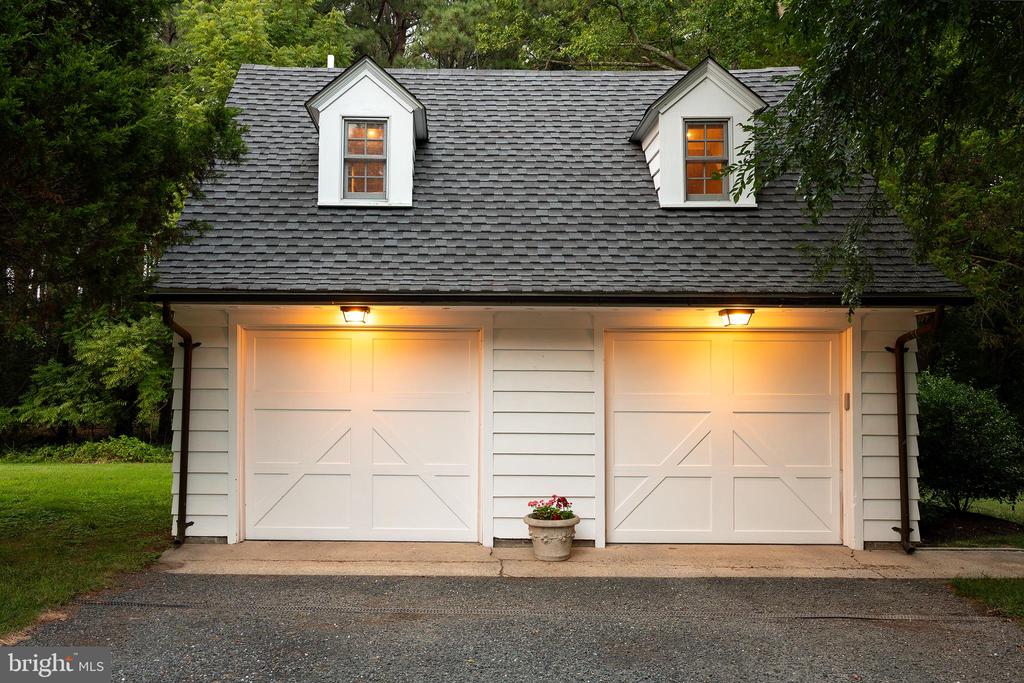 Detached two-car garage with white doors, two roof dormers, and warm exterior lights.