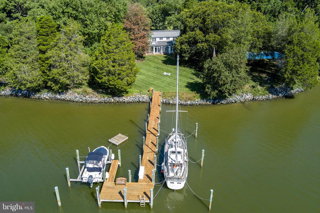 Waterfront home with a long dock, two boats, wooded grounds, and a swimming pool.