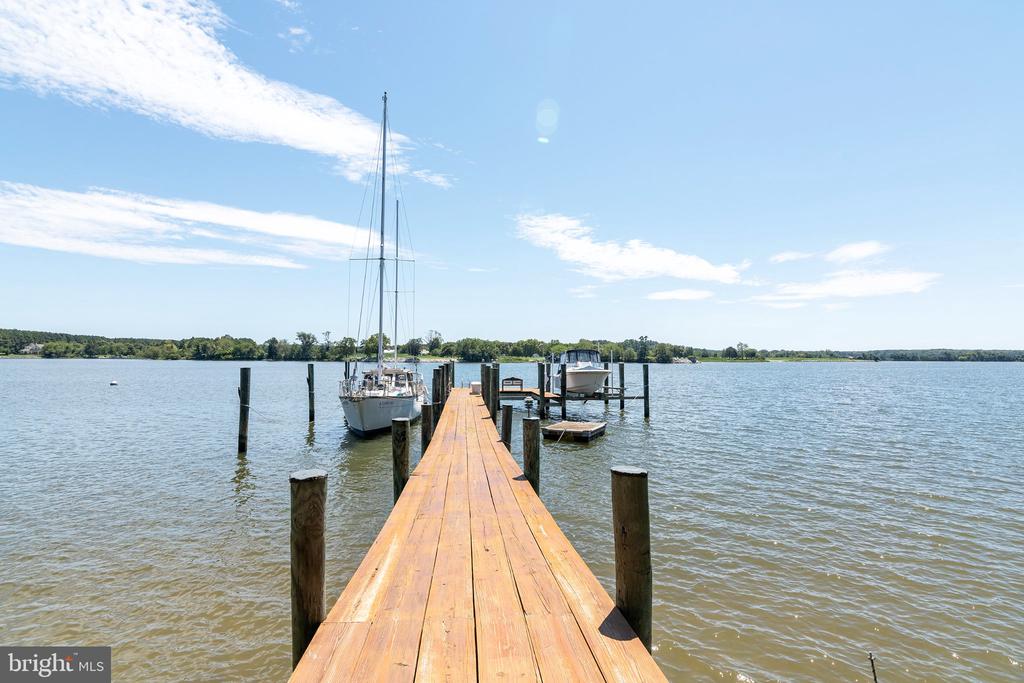 Wooden dock extending into the water, with a sailboat and motorboat moored beside it.