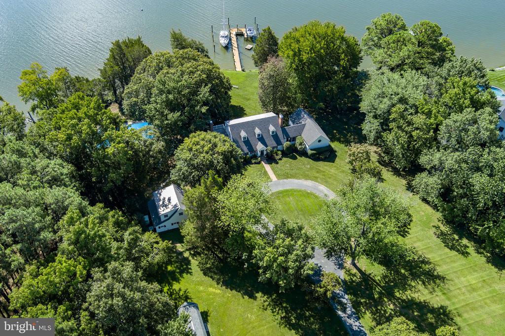 Waterfront home surrounded by mature trees, with a broad lawn and private dock.