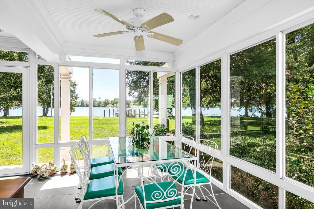 Waterfront sunroom with a glass dining table, teal-cushioned chairs, and expansive windows.