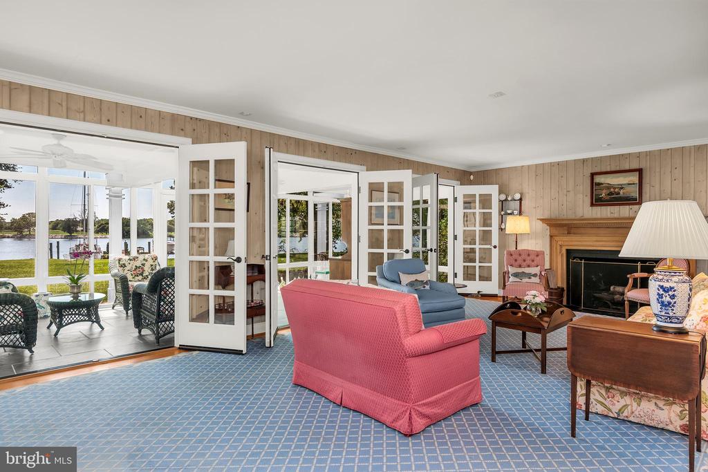 Living room with a wood fireplace and open French doors overlooking the water.