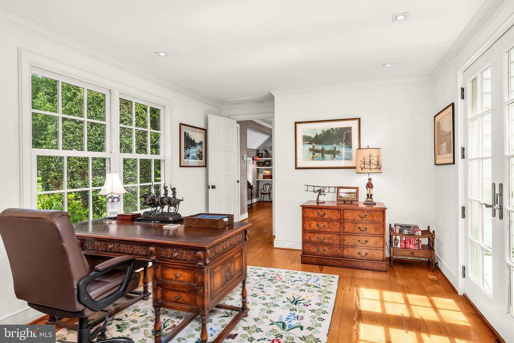 Home office with carved wooden desk, hardwood floors, and large windows overlooking greenery.