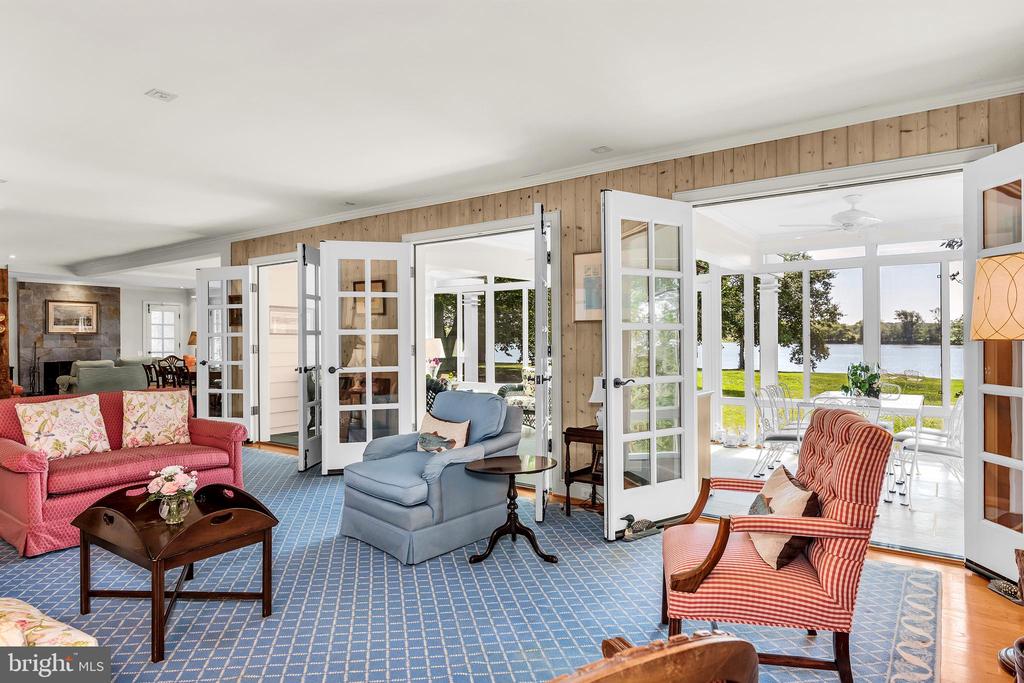 Furnished living room with open French doors overlooking a sunroom and water.