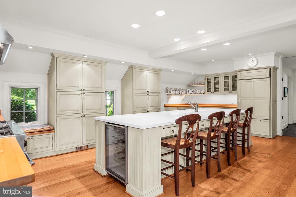 Kitchen with a large white island, cream cabinets, wooden bar stools, and hardwood floors.