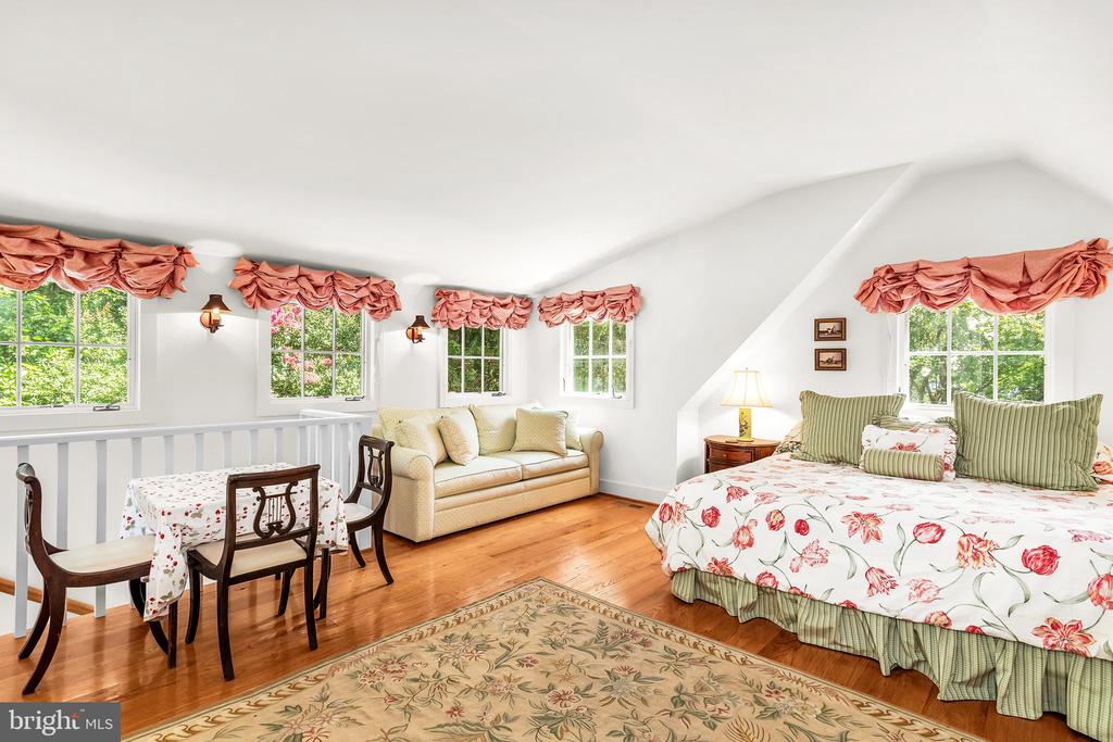 Bedroom with floral bedding, a cream sofa, and a dining table beneath a sloped ceiling.