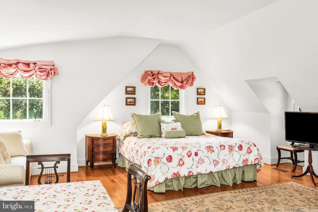 Bedroom with a floral bedspread, green pillows, and windows beneath a sloped ceiling.