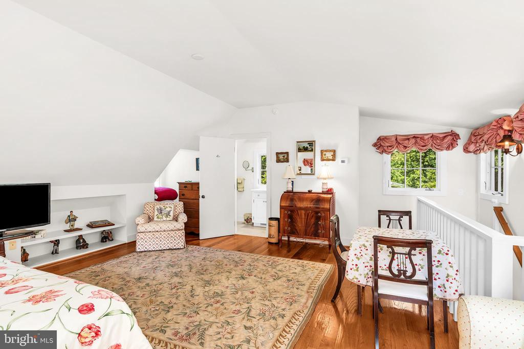 Furnished upper-level bedroom with sloped ceilings, floral rug, and a small table by the railing.