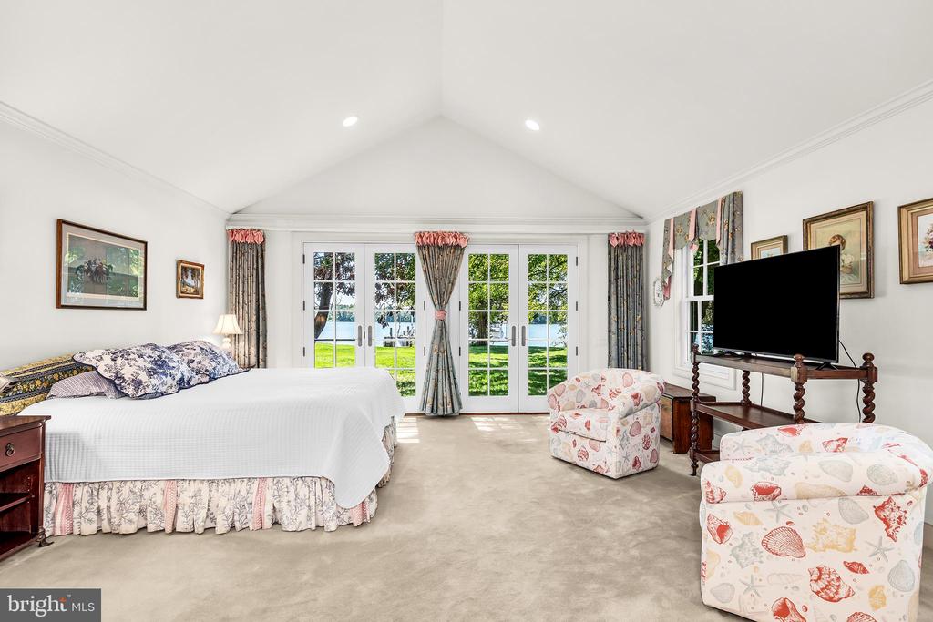 Furnished bedroom with French doors overlooking a lawn and water.