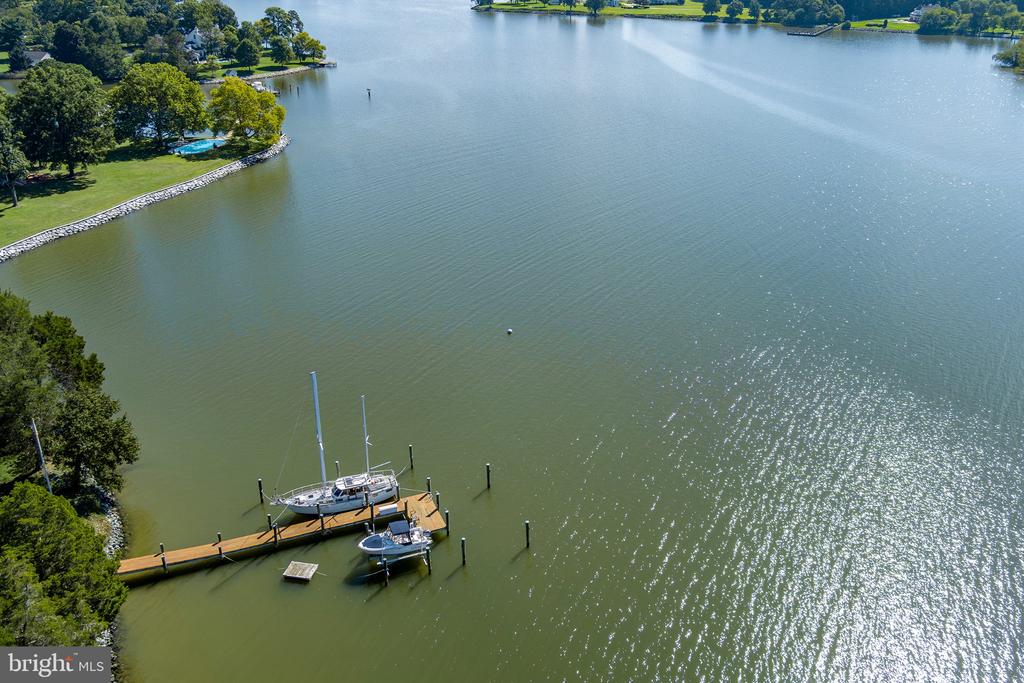 Aerial view of a waterfront dock with two sailboats and a motorboat beside a tree-lined shore.