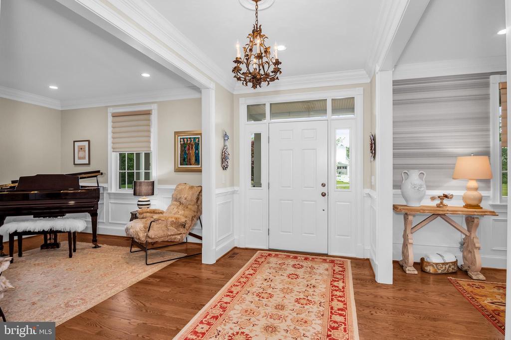 Furnished entry foyer with white front door, patterned runner, chandelier, and a grand piano nearby.