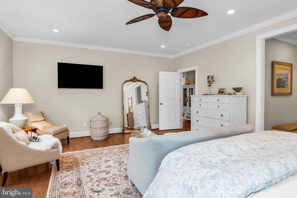 Bedroom with a pale blue bench, white dresser, patterned rug, and ceiling fan.