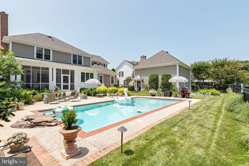 Home’s backyard with a rectangular swimming pool, screened porch, patio seating, and landscaped lawn.