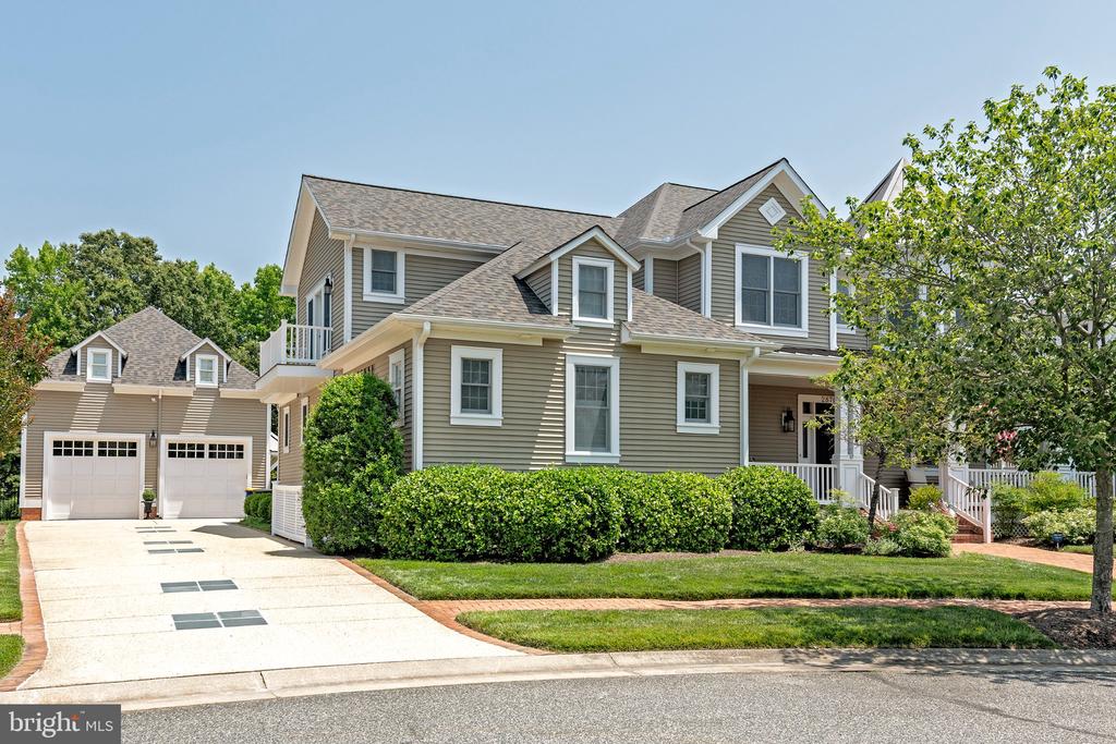 Two-story taupe house with a covered porch, landscaped shrubs, and a driveway to a two-car garage.