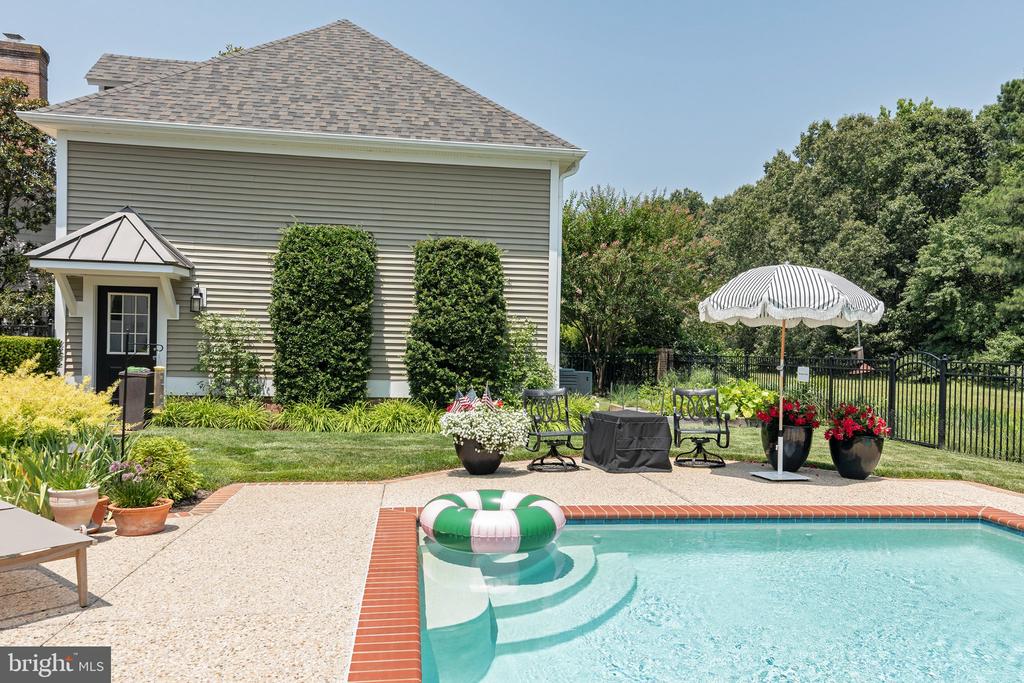 Backyard pool with a brick edge, patio seating, and a striped umbrella beside the house.