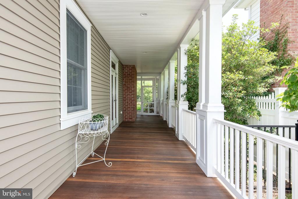 Covered porch with dark wood flooring, white columns and railing, and a white metal chair.