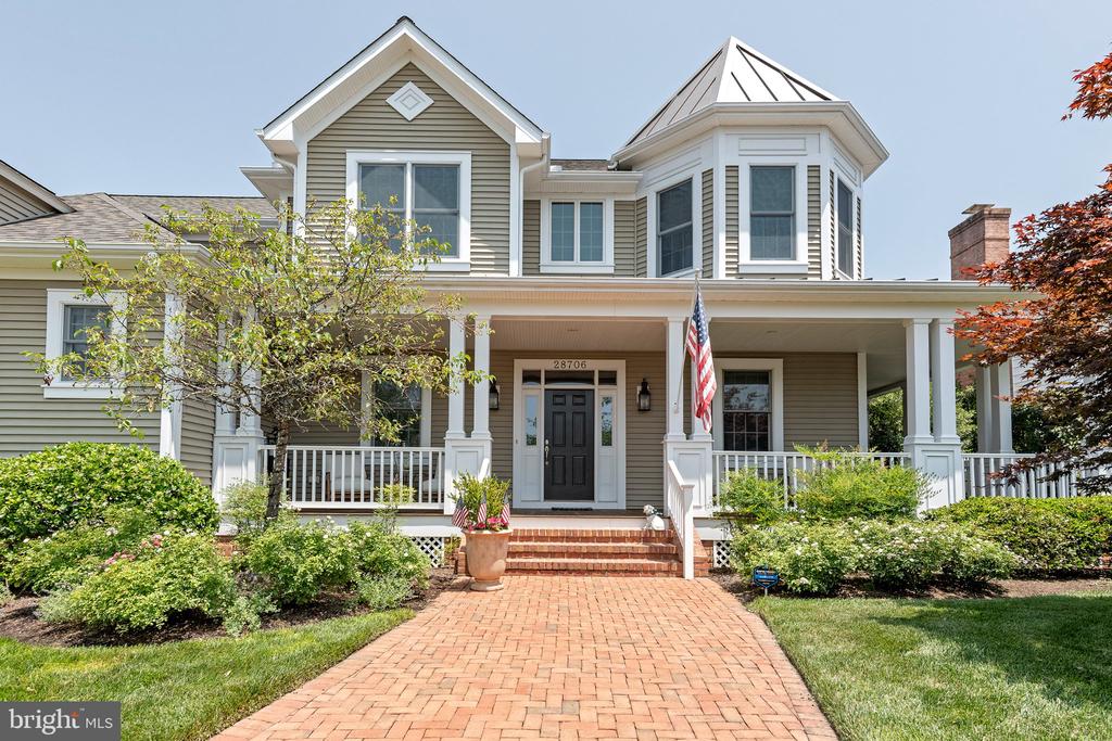 Gray two-story home with a covered porch, brick walkway, and American flag by the entrance.