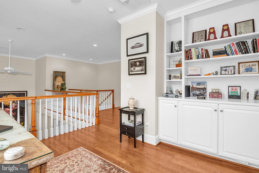 Upstairs library with built-in bookshelves, hardwood floors, and a wooden stair railing.