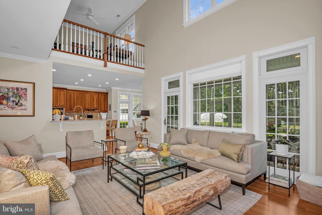 Living room with vaulted ceiling, upstairs balcony railing, gray sectional, and open kitchen.