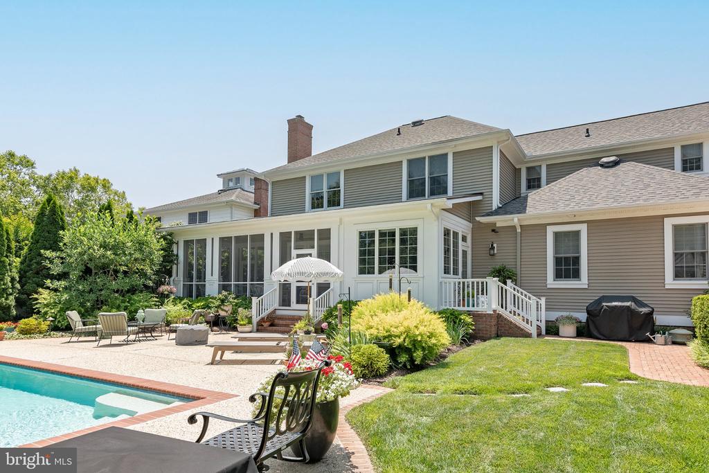 Home’s rear exterior with a screened porch, swimming pool, patio seating, and landscaped lawn.