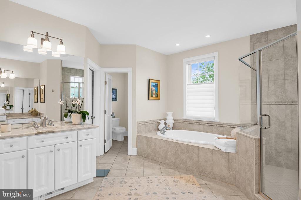 Primary bathroom with double vanity, tiled soaking tub, and glass-enclosed shower.