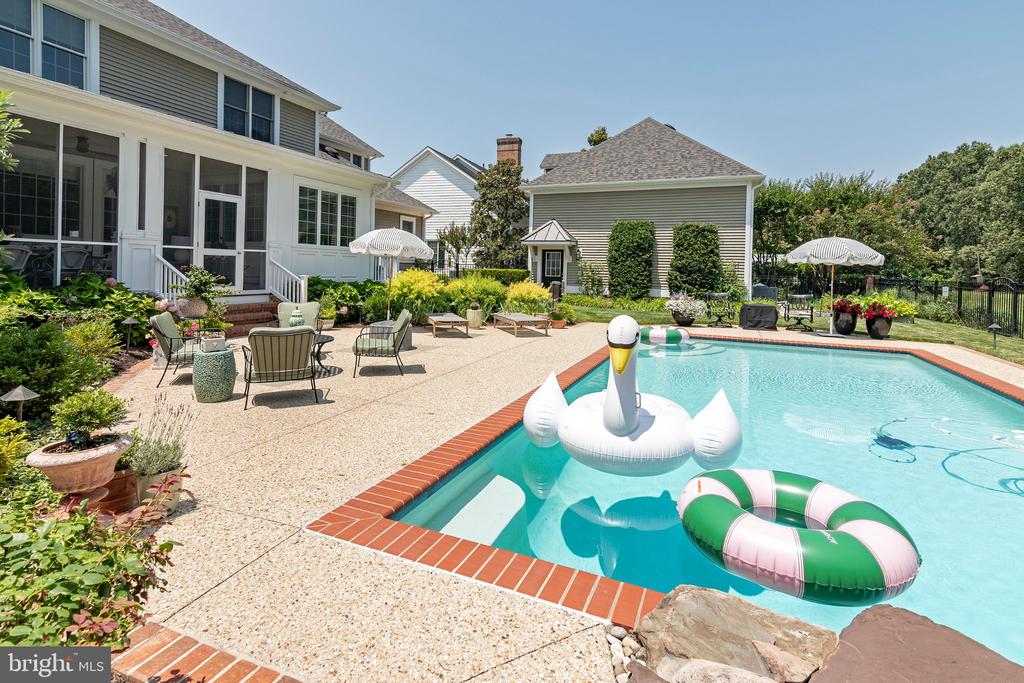 Backyard pool beside a furnished patio, with colorful floats and a detached outbuilding.