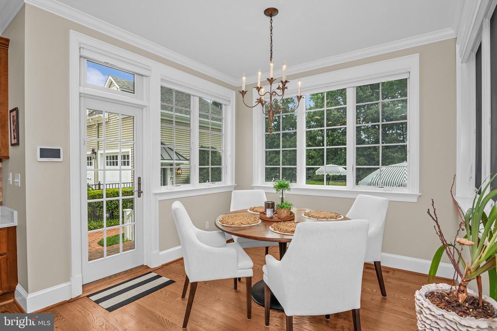 Dining area with a round table, white chairs, chandelier, and large garden-facing windows.
