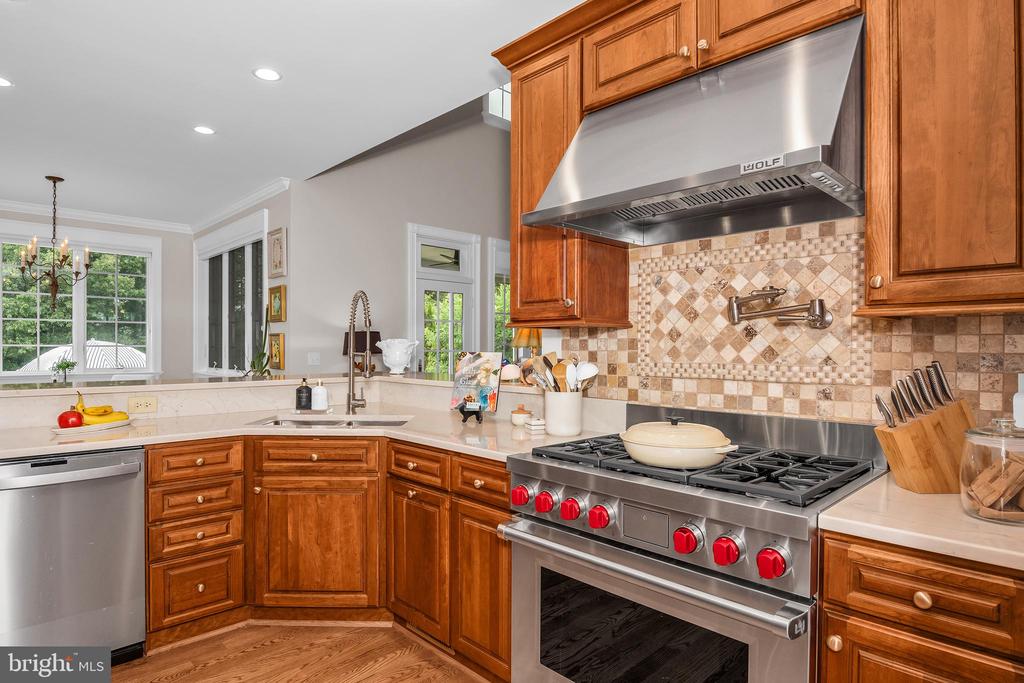 Kitchen with warm wood cabinetry, stainless steel gas range, patterned tile backsplash, and a window over the sink.