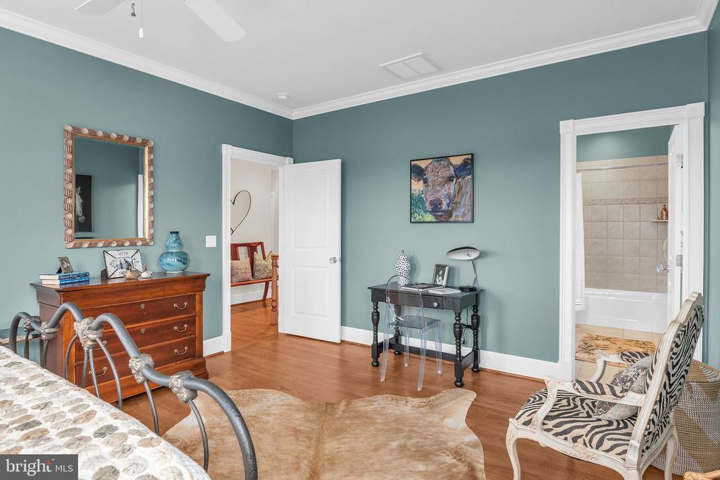 Bedroom with teal walls, hardwood floors, a metal bed, and an open doorway to a tiled bathroom.