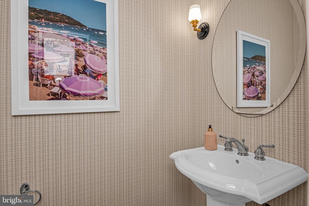 Bathroom pedestal sink with chrome faucets, oval mirror, and framed beach artwork.