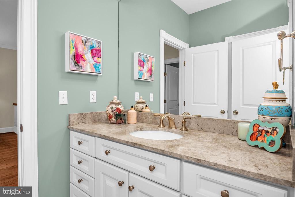 Bathroom vanity with a beige stone countertop, brass faucet, and pale green walls.
