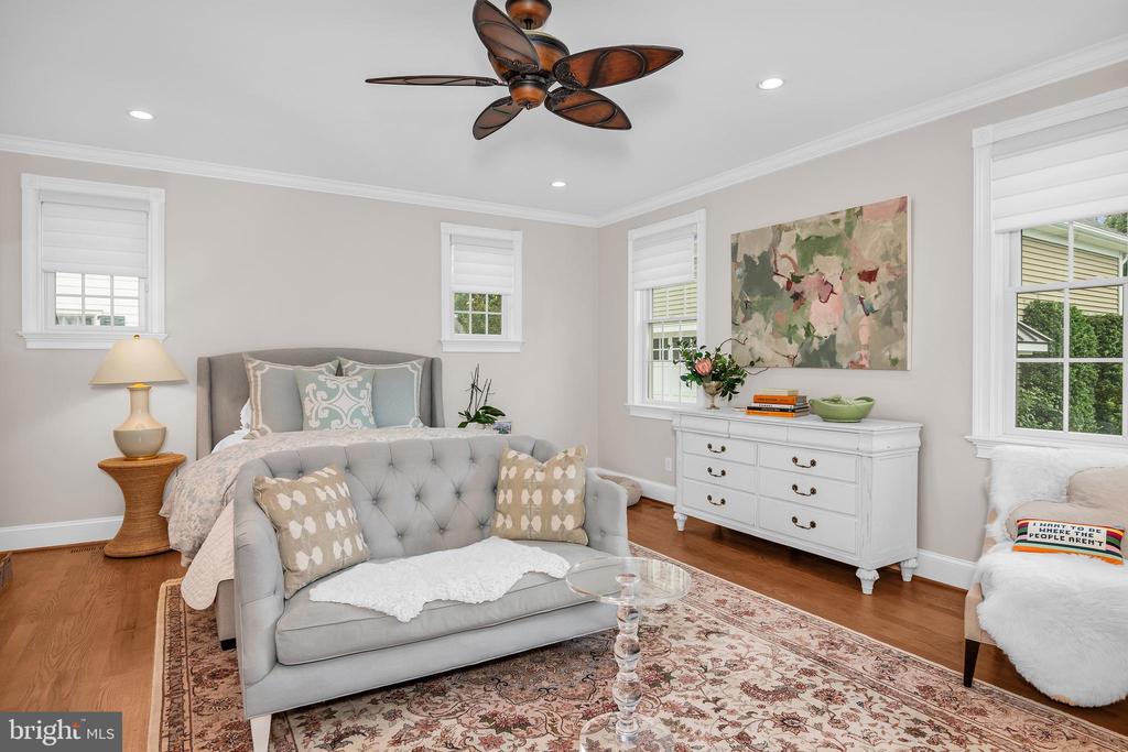 Staged bedroom with a gray bed, tufted loveseat, white dresser, and patterned rug.
