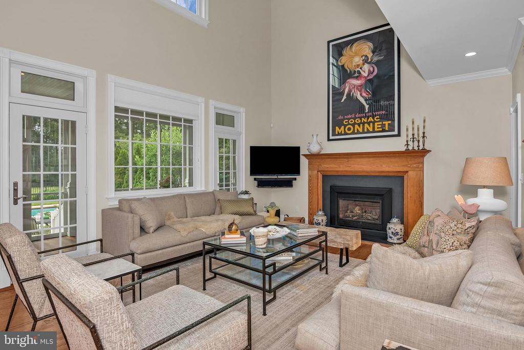 Furnished living room with beige seating, large windows, and a wood-framed fireplace.