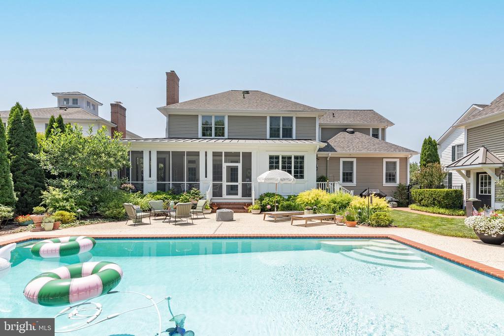 Swimming pool beside a two-story home with a screened porch and furnished patio.