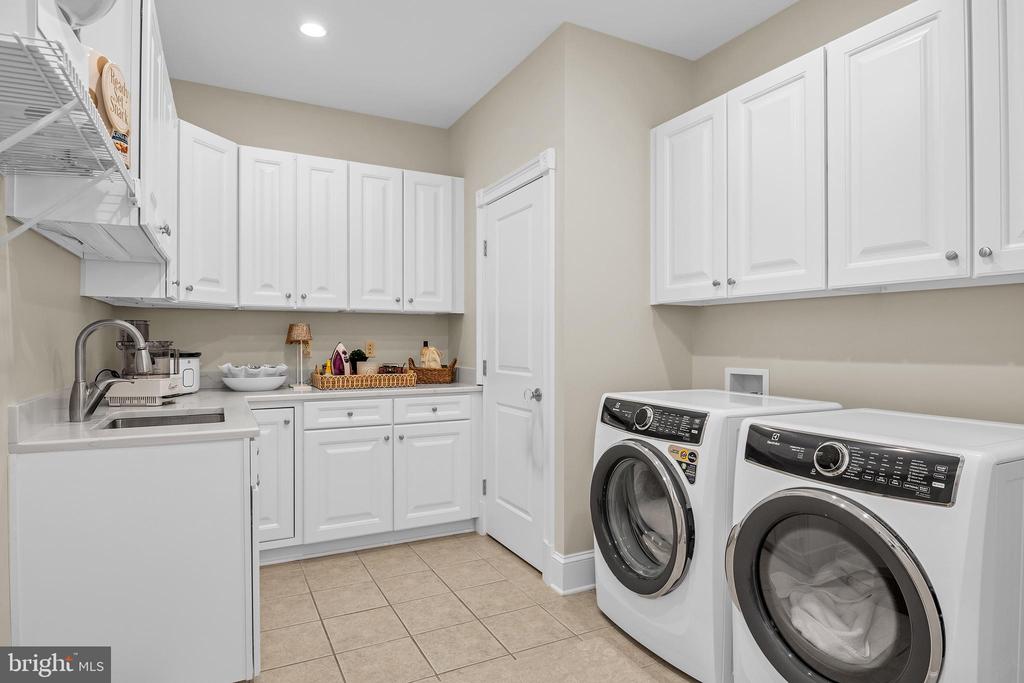 Laundry room with white cabinetry, a utility sink, and front-loading washer and dryer.