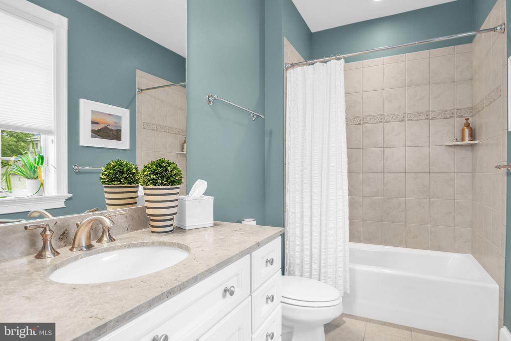 Bathroom with a white vanity and tiled tub-shower beneath teal walls.