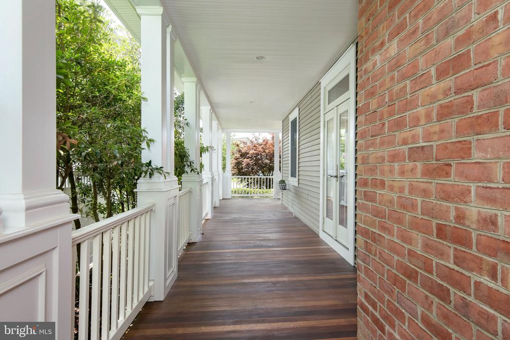 Covered porch with dark wood decking, white columns and railings, and a brick wall.