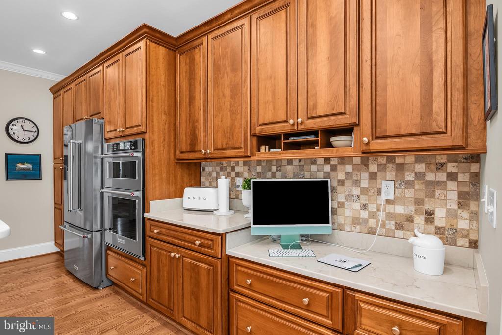 Kitchen with extensive wood cabinetry, tiled backsplash, stainless refrigerator, and double wall ovens.