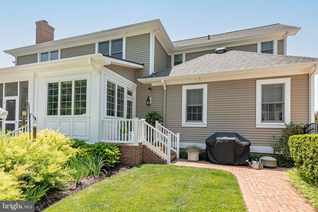 Home’s rear exterior with a white enclosed sunroom and brick-paver walkway.