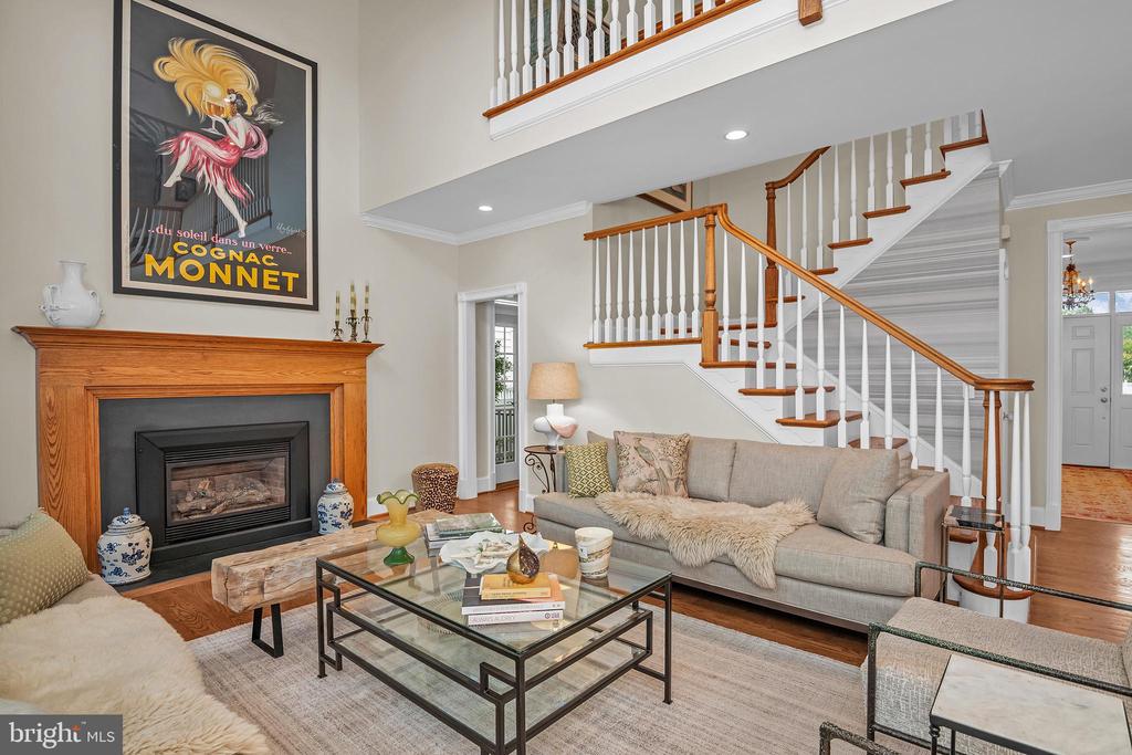 Staged living room with a wood-mantel fireplace, gray sofa, and prominent staircase.