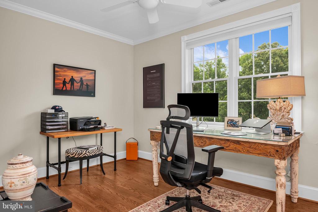 Home office with an ornate wooden desk beside large windows overlooking trees.